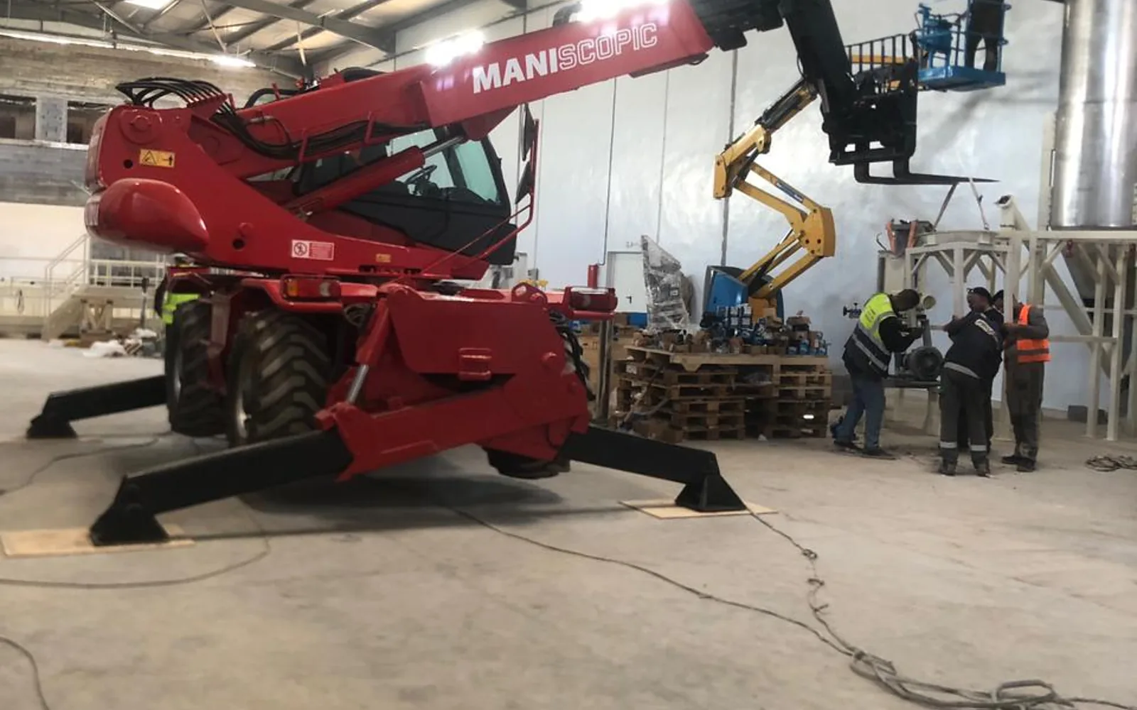 Chariot télescopique rotatif Manitou sur stabilisateurs dans un hall industriel