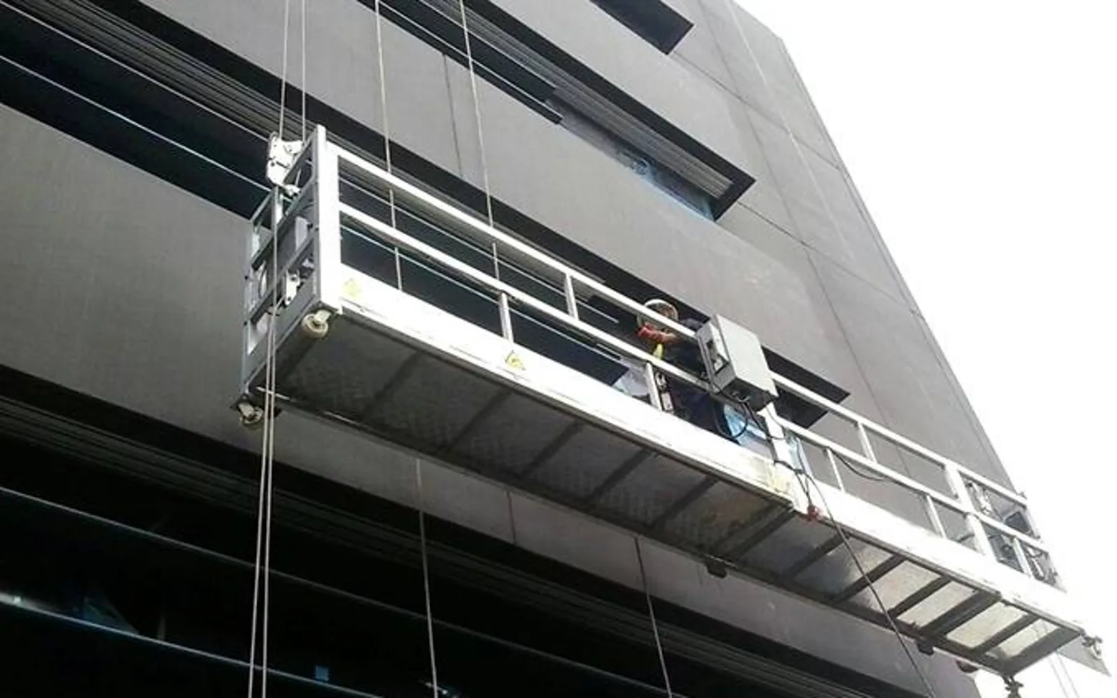 Plateforme suspendue en aluminium EasyMat le long d'une façade, opérateur au travail